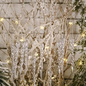 Set of transparent acrylic icicle ornaments hanging on a snowy Christmas tree with warm lights