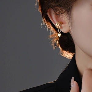 Detailed view of layered gold ear cuff with three rings and a heart pendant on ear