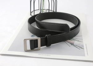Close-up of black faux leather belt with a matte silver square buckle on magazines