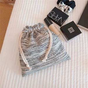 Detailed close-up of woven tweed drawstring pouch with cosmetics on a white striped background