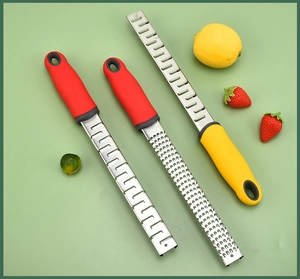 Flat lay of stainless steel kitchen graters with red and yellow handles on green background