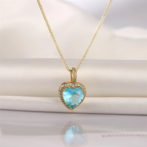 Detailed view of heart-shaped gold necklace with blue gemstone and pavé zircon inlay