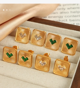 Close-up of gold square stud earrings with heart-shaped emerald and zircon stones