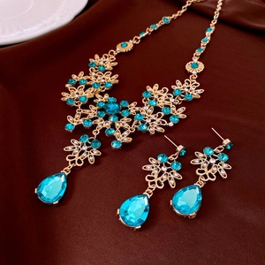 Detailed close-up of gold flower necklace and earrings set with blue teardrop crystals