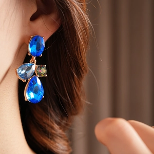 Detail of vintage geometric earrings with blue teardrop crystals worn by a model