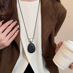 Collier pendentif ovale noir et argent minimaliste porté sur un blazer marron