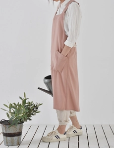 Side view of a full-length pink linen gardening apron with a large front pocket and straps