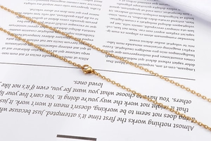 Detailed view of a gold 18k titanium steel cable chain necklace with lobster clasp on a book