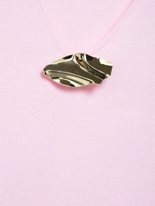 Detail of a pink knit top featuring a modern gold irregular wave metal brooch accessory