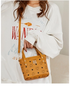 Detail of yellow bucket bag with monogram print and gold studs on leather handle