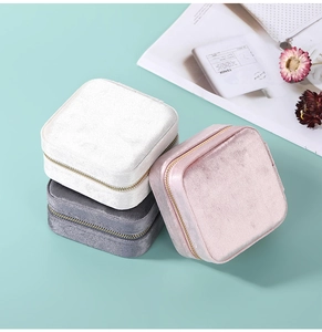 Velvet jewelry organizers in white, gray, and pink with gold zippers on green background