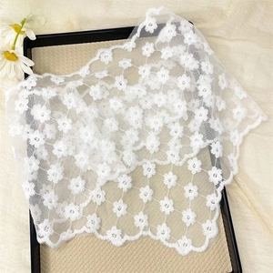 Detail of white daisy floral embroidery on delicate lace fabric with scalloped edges