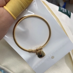 Gold cable twist bangle with heart pendant charm in professional packaging for women