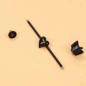 Macro detail of black industrial barbell with heart and wing charms on beige background