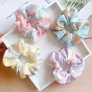 Detail of four colorful tie-dye mesh hair scrunchies on a white tray with green leaves