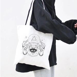 Detail of a white canvas tote bag with Demon Eye print carried by a model in black hoodie