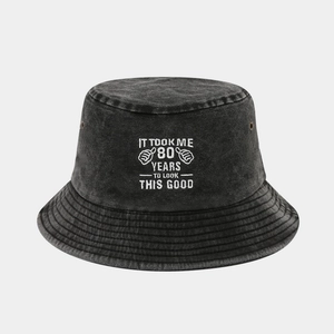 Dettaglio di cappello a secchiello in cotone con ricamo '80 YEARS' e occhielli metallici