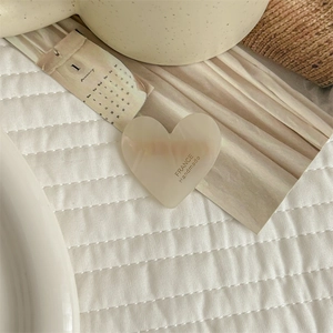 Detail view of a cream heart acetate hair clip on quilted fabric with a ceramic cup