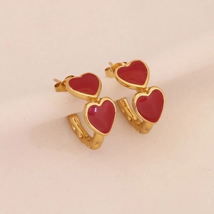Golden C-shaped stainless steel earrings with red enamel heart detail on cream background