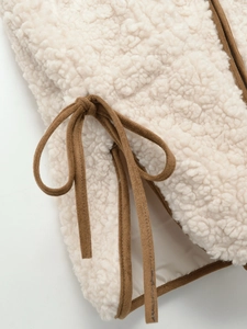 Detail of cream sherpa vest featuring contrast brown piping and side tie-up ribbons
