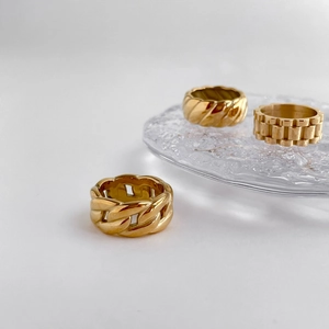 Drei goldene Ringe mit Ketten- und Texturdesign auf einem Glasblock präsentiert