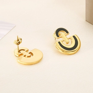 Close-up of golden C-shaped stainless steel earrings with black enamel inlay