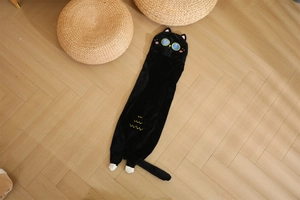 Detailed view of black cat long plush pillow on wooden floor in warm home setting