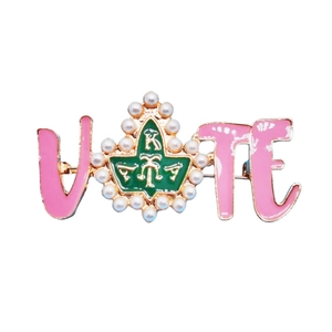 Pink VOTE alphabet brooch with green enamel crest and pearl accent on white background