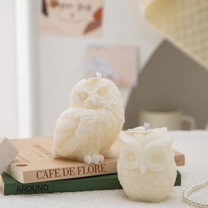 Detailed close-up of cream owl scented candles with intricate carved feather texture on books