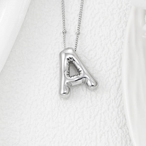 Macro shot of 3D puffy silver letter A pendant on delicate chain over white satin fabric