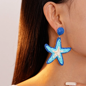 Dettaglio degli orecchini a stella marina in rafia intrecciata blu e crema su modella