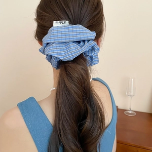 Close-up of blue plaid scrunchie with soft fabric pleats and small brand woven label