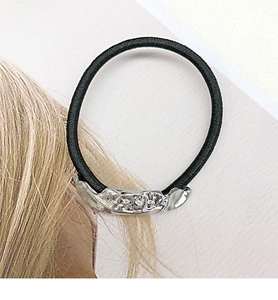 Detail of black elastic hair tie featuring a silver textured wavy metal ornament