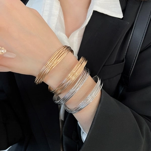 Close-up of stacked gold and silver thin wire bracelets worn over a black blazer sleeve