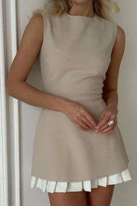 Détail d'une mini robe beige sans manches avec ourlet plissé blanc et coupe ajustée chic
