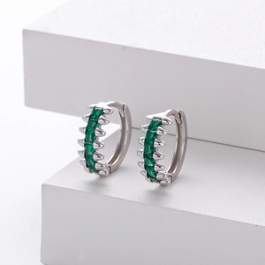 Macro shot of silver hoop earrings featuring emerald green stones in a claw setting