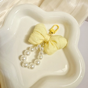 Detail of a yellow bow keychain with white pearls and plastic clasp on a ceramic tray