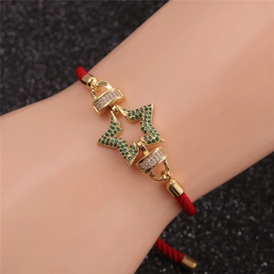 Détail d'une breloque étoile dorée sur un bracelet tressé rouge avec des zircons verts