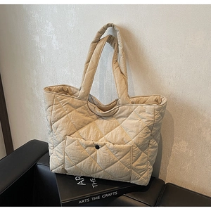 Detail shot of beige quilted tote bag showing diamond stitching and front snap pocket