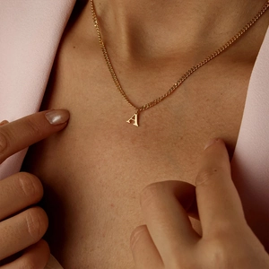 Detail of a minimalist gold stainless steel necklace with a letter A pendant.