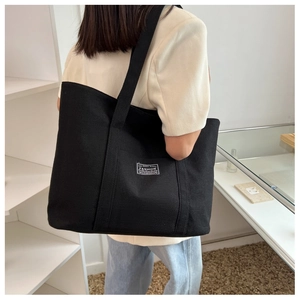 Detail of minimalist black canvas tote bag showing size and wide shoulder strap on model