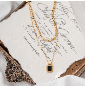 Detail of a gold double-layer necklace with a sleek black rectangular pendant on silk