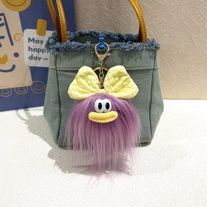Dettaglio del portachiavi mostro viola di peluche con fiocco giallo su borsa di jeans