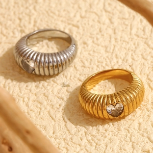 Detail of gold and silver textured rings with heart shaped zircon on stone surface