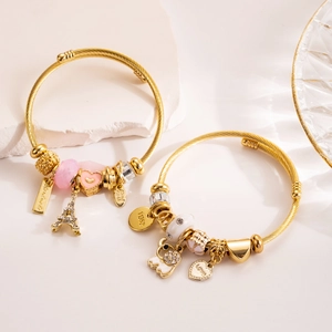 Two gold heart charm bracelets featuring Eiffel Tower and Love pendants on stone