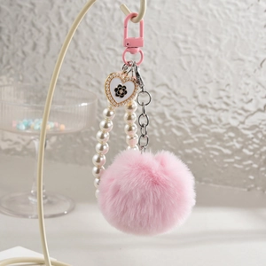 Porte-clés à pompon rose et perles avec pendentif cœur sur un présentoir beige
