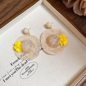 Macro detail of raffia straw hat earrings with yellow floral accents on display tray