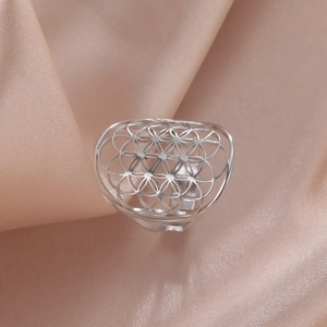 Close-up of silver hollow floral geometric ring on soft pink satin fabric background