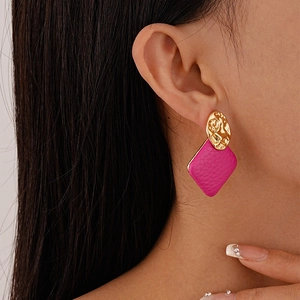 Detail of gold hammered round metal and fuchsia leather rhombus earrings on model