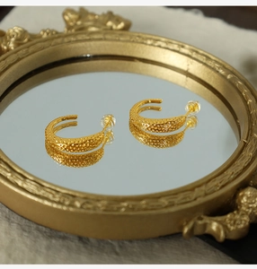 Detailed view of C-shaped gold-plated earrings with unique hammered dot texture on a mirror